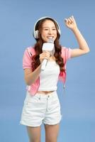 Happy young Asian woman singing with microphone sing and headphone over blue background. photo