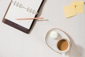 cuaderno limpio, taza de café y macaron colorido en la vista superior del escritorio gris. acogedor desayuno matutino. endecha plana de moda. macarrones dulces. foto