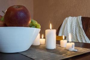 burning candles and a vase with fruit apples and grapes on the table near the lamp photo