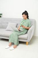 Shot of pretty young woman using her mobile phone while working with laptop sitting on sofa at home. photo