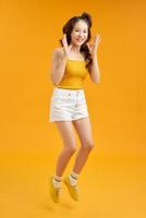 Full length portrait of a cheerful young asian woman celebrating success while jumping isolated over yellow background photo