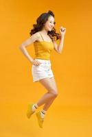 Joyful young asian girl having fun fooling around jumping doing winner gesture on yellow background. photo