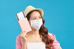 Young woman traveller wearing handmade cotton face mask with passport and ticket on blue background. Trip concept during coronavirus. photo
