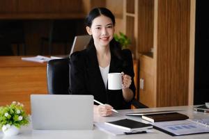 Company employees are sitting at work using computers, tablets and documents in their work. photo