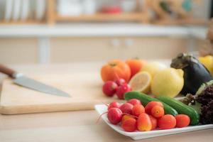 los tomates cherry se colocan en una bandeja con rábanos, pepinos, lechuga roja y otras frutas y verduras. como materia prima para hacer ensaladas en la mesa de la cocina. foto