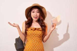 Image of excited brunette woman 20s wearing straw hat while holding passport with travel tickets isolated over beige background photo