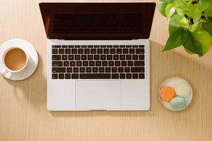 Laptop, colored macaroons cookies, cup of coffee with notebook on wooden table. Top view. Flat lay photo