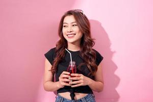 portrait of beautiful happy cute woman girl in casual  summer clothes drink red soda water from bottle with straw over pink background photo