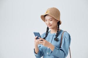 mujer sonriente de moda usando un teléfono inteligente con sombrero de paja sobre fondo blanco, foto