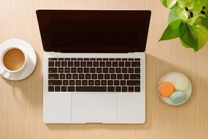 Laptop, colored macaroons cookies, cup of coffee with notebook on wooden table. Top view. Flat lay photo