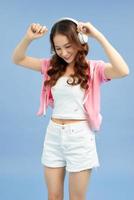 Amazing charming summer young woman in jeans shorts over colorful blue background. Dancing, listening to music with headphones photo