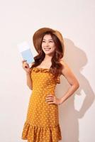 A young woman in a orange polka dots dress with a straw hat on her head is holding a passport and plane tickets photo