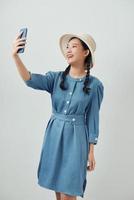 Happy beautiful girl in casual or hipster style, pigtail hairstyle, standing, holding mobile smart phone and doing selfie photo