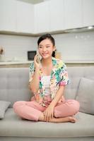 Slender young woman relaxing at home on a sofa chatting on her mobile phone with a happy smile photo