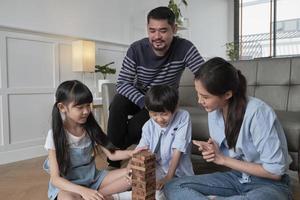 Happy Asian lovely Thai family activity, parents, dad, mum, and children have fun playing and joyful wooden toy blocks together on living room floor, leisure weekend, and domestic wellbeing lifestyle. photo