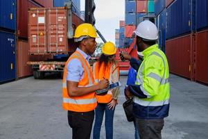 los trabajadores afroamericanos y los equipos con uniformes de seguridad y cascos usan walkie-talkies, trabajan en grúas logísticas con pilas de contenedores, control de carga, envío de mercancías e industria de transporte de carga. foto