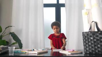 Young girl in red dress plays with markers at a table drawing in notebook video