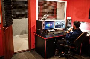 Young asian singer with microphone recording song in record music studio with sound producer. photo