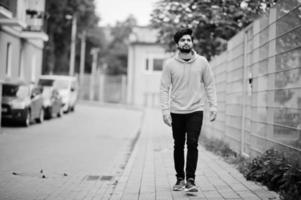 Urban young hipster indian man in a fashionable yellow sweatshirt. Cool south asian guy wear hoodie walking on fall street. photo