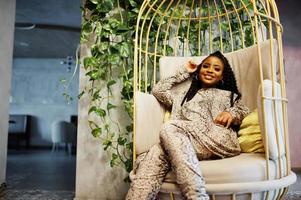 Young stylish african american woman in gold bird cage pose indoor. photo