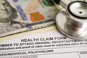 Health claim form with stethoscope and US dollar banknotes, insurance accident medical concept.
