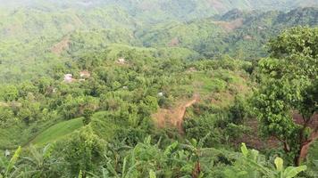 Aerial drone shot of hilly areas and small houses. Hilly hiking trail 4K footage with large hill area and small residences. Landscape mountain view with green hilly jungle roads. video