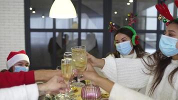 pessoas em uma festa natalícia usam chapéus e máscaras festivas e brindam com bebidas sobre a mesa video