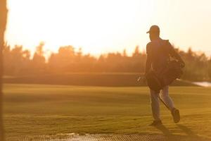 golfer  walking and carrying golf  bag at beautiful sunset photo