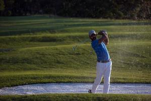 golfer hitting a sand bunker shot on sunset photo