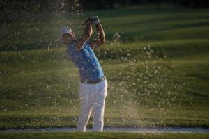 golfer hitting a sand bunker shot on sunset photo