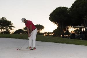 golfista golpeando un tiro de búnker de arena al atardecer foto