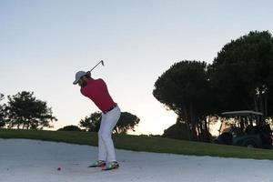 golfista golpeando un tiro de búnker de arena al atardecer foto