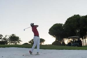 golfer hitting a sand bunker shot on sunset photo