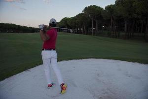 golfer hitting a sand bunker shot on sunset photo