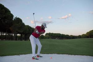 golfer hitting a sand bunker shot on sunset photo