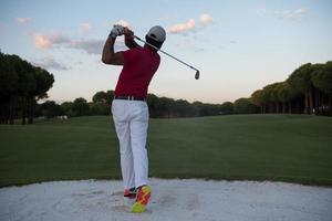 golfer hitting a sand bunker shot on sunset photo