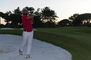 golfista golpeando un tiro de búnker de arena al atardecer foto