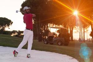 golfer hitting a sand bunker shot on sunset photo