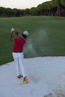 golfer hitting a sand bunker shot on sunset photo