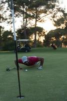 jugador de golf que sopla la pelota en el agujero con la puesta de sol en el fondo foto