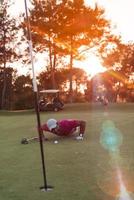 jugador de golf que sopla la pelota en el agujero con la puesta de sol en el fondo foto