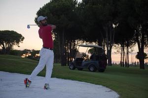 golfista golpeando un tiro de búnker de arena al atardecer foto