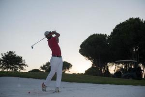 golfista golpeando un tiro de búnker de arena al atardecer foto