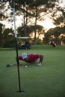 golf player blowing ball in hole with sunset in background photo