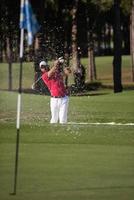 golfista golpeando un tiro de búnker de arena foto