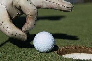 man's hand putting golf ball in hole photo