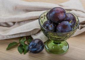 Ripe fresh plum in a bowl on wooden background photo