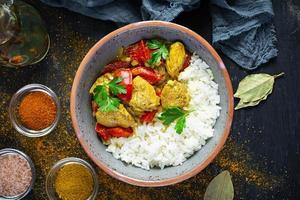 Spicy chicken curry with rice. Curry sauce with chicken and rice on dark background. Top view photo