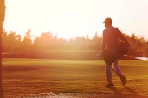 golfer  walking and carrying golf  bag at beautiful sunset photo