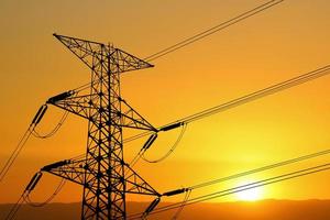 Silhouette of high voltage poles with electric wires. Silhouette of high voltage power line cables in an orange evening sunset. Steel structure of electric poles. electric power transmission concept photo